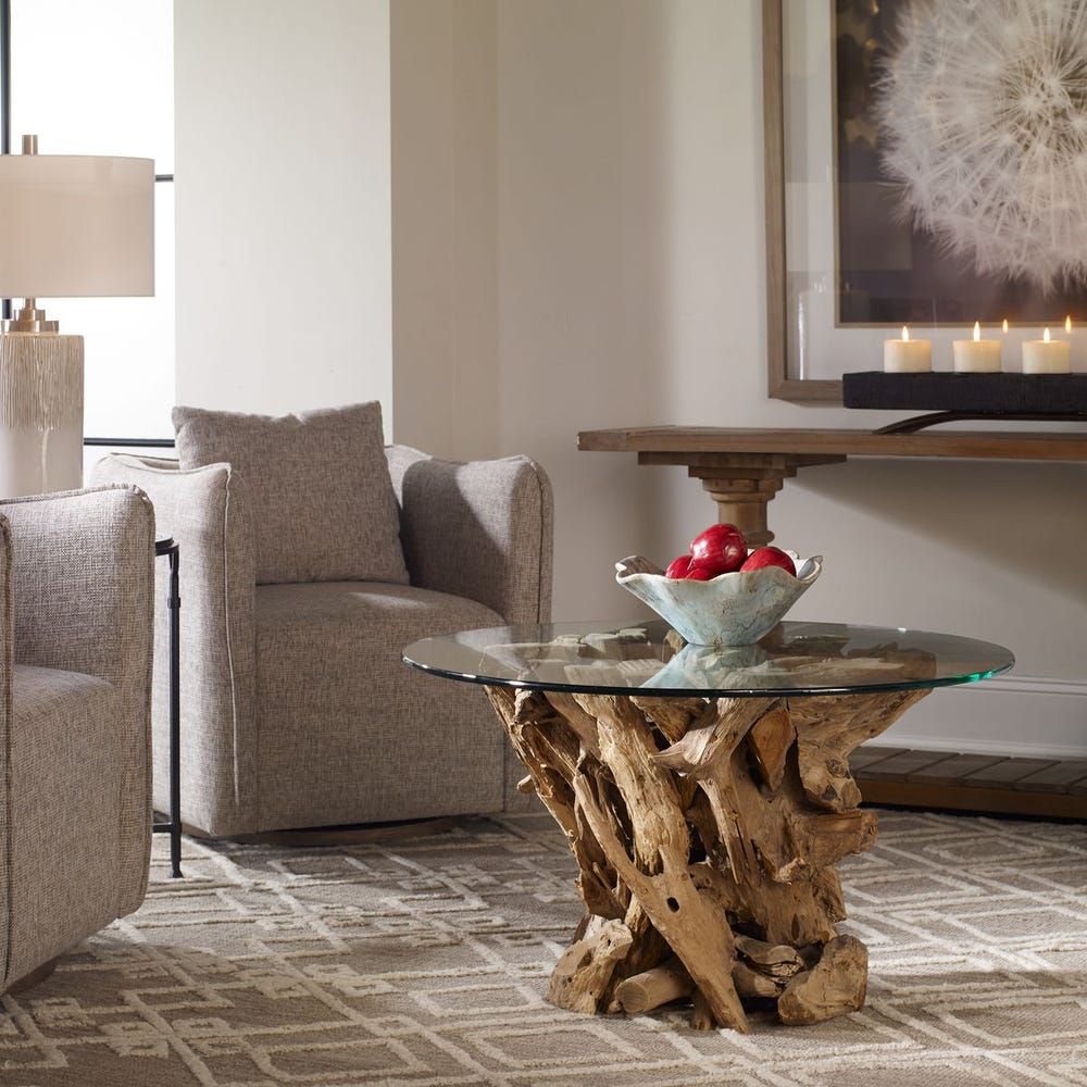 Round glass top coffee table with driftwood base, in a living room setting.
