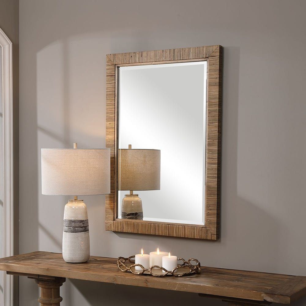 Wooden framed mirror above a rustic table with lamps and candles, against a gray wall.