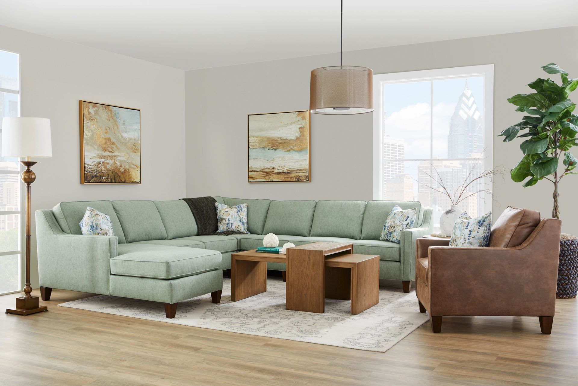 A light green sectional sofa, a brown armchair, and a wooden coffee table in a living room with art and a tall plant.