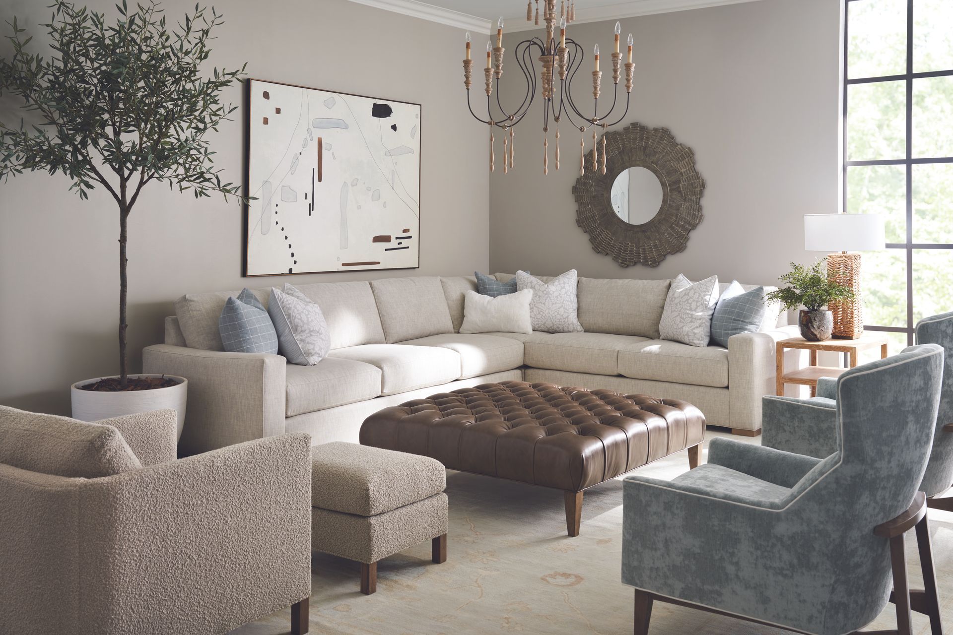 A living room with beige sectional sofa, armchairs, and tufted ottoman. Neutral colors, natural light.