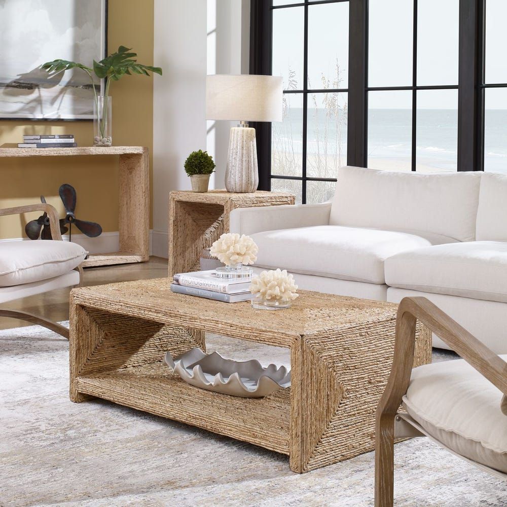 Living room with white sofa, woven coffee table, and neutral rug. Ocean view in the background.