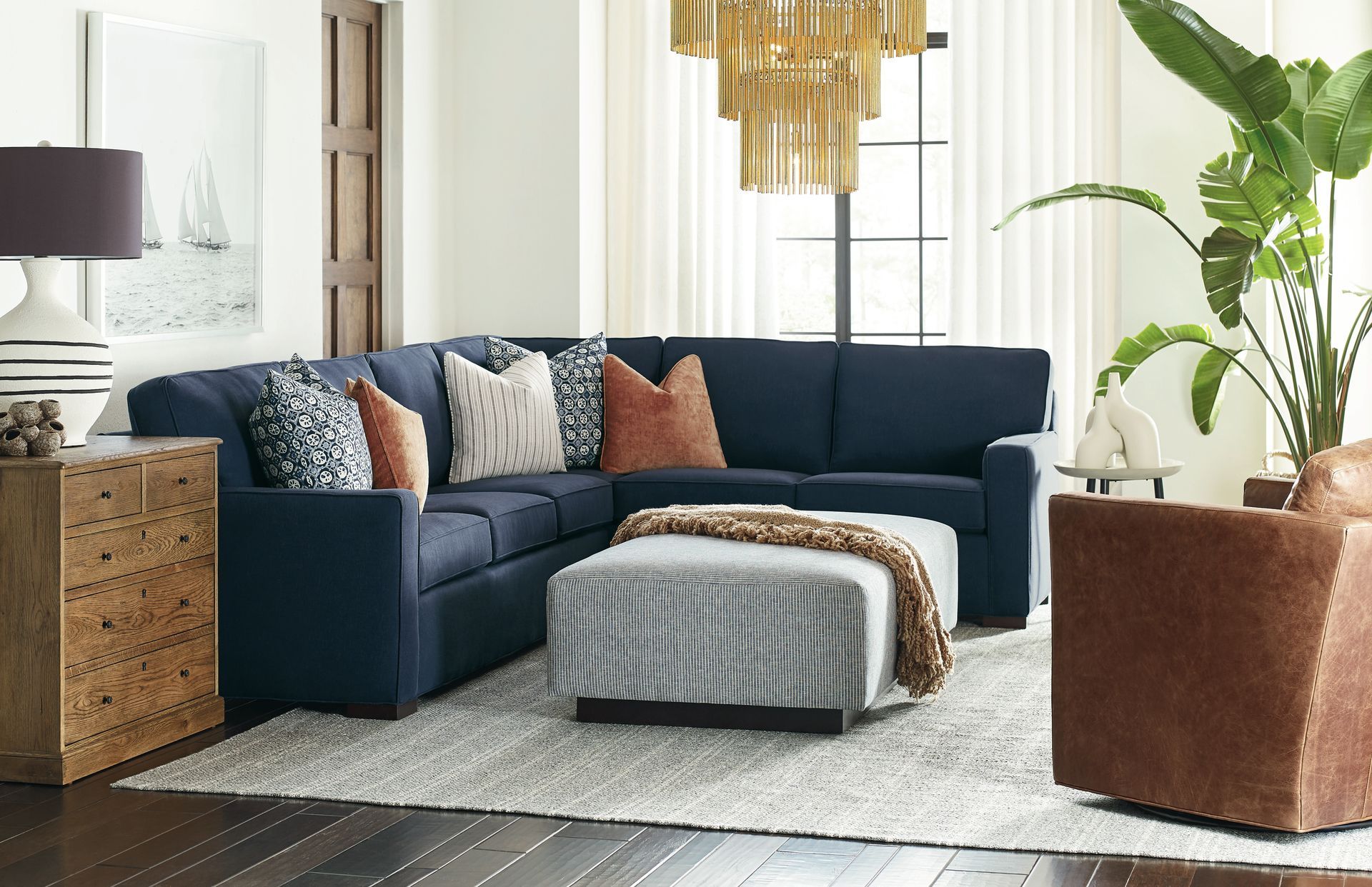 Living room with navy blue sectional, patterned pillows, ottoman, and large plant.