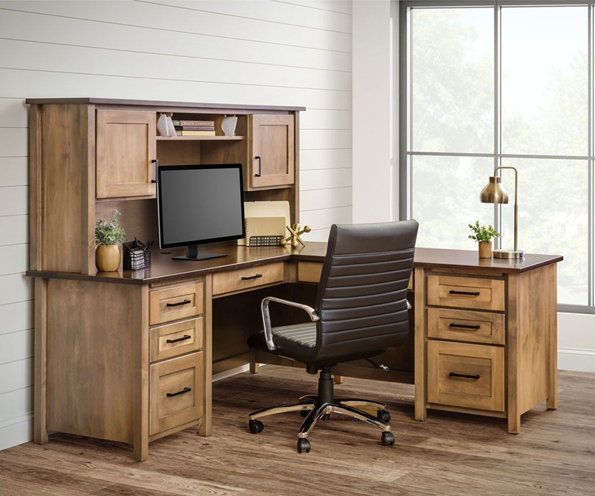 Wooden L-shaped desk with hutch, chair, and window. Brown desk, black monitor, and leather chair in a room.