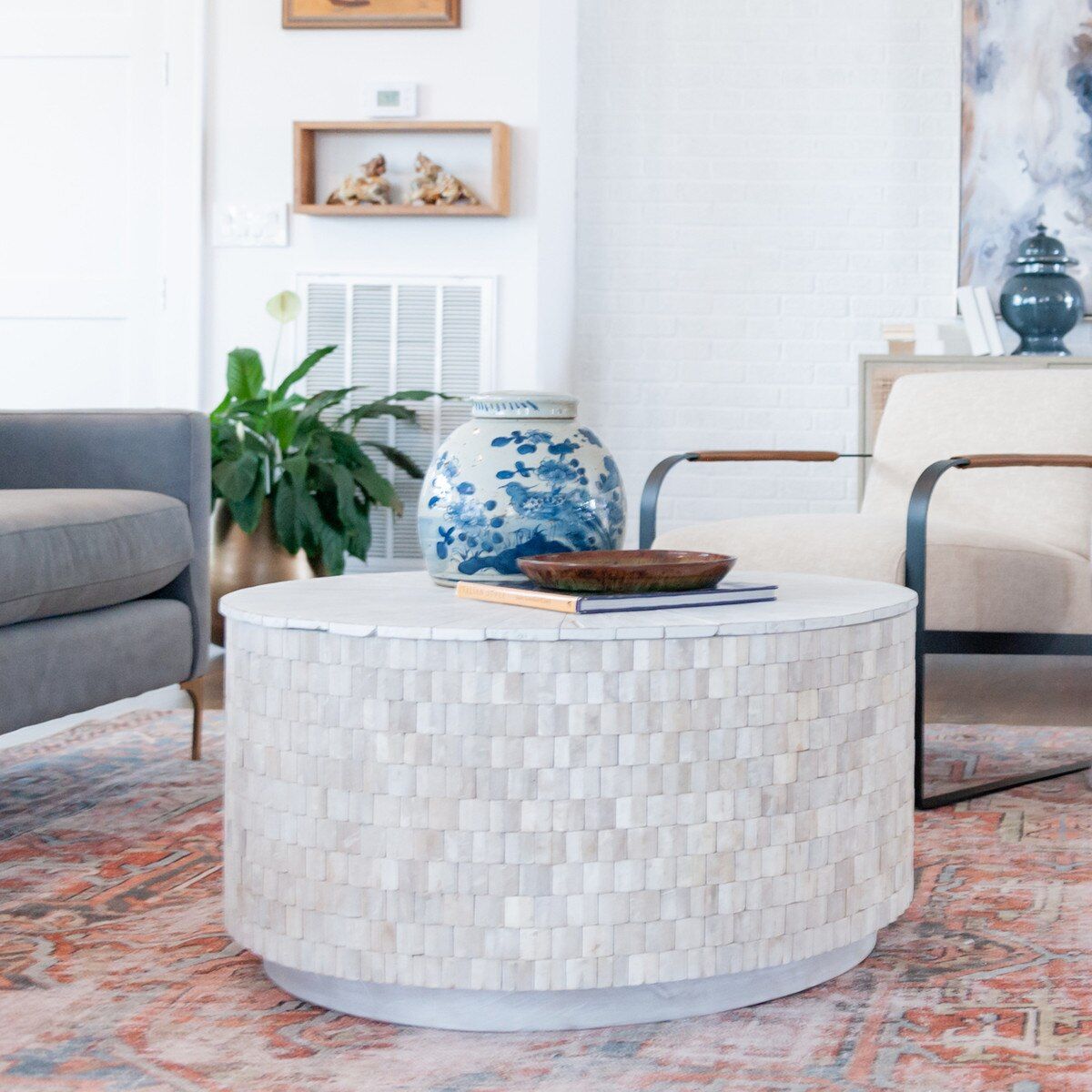 Round mosaic tile coffee table with blue and white vase, wooden bowl, and rug.