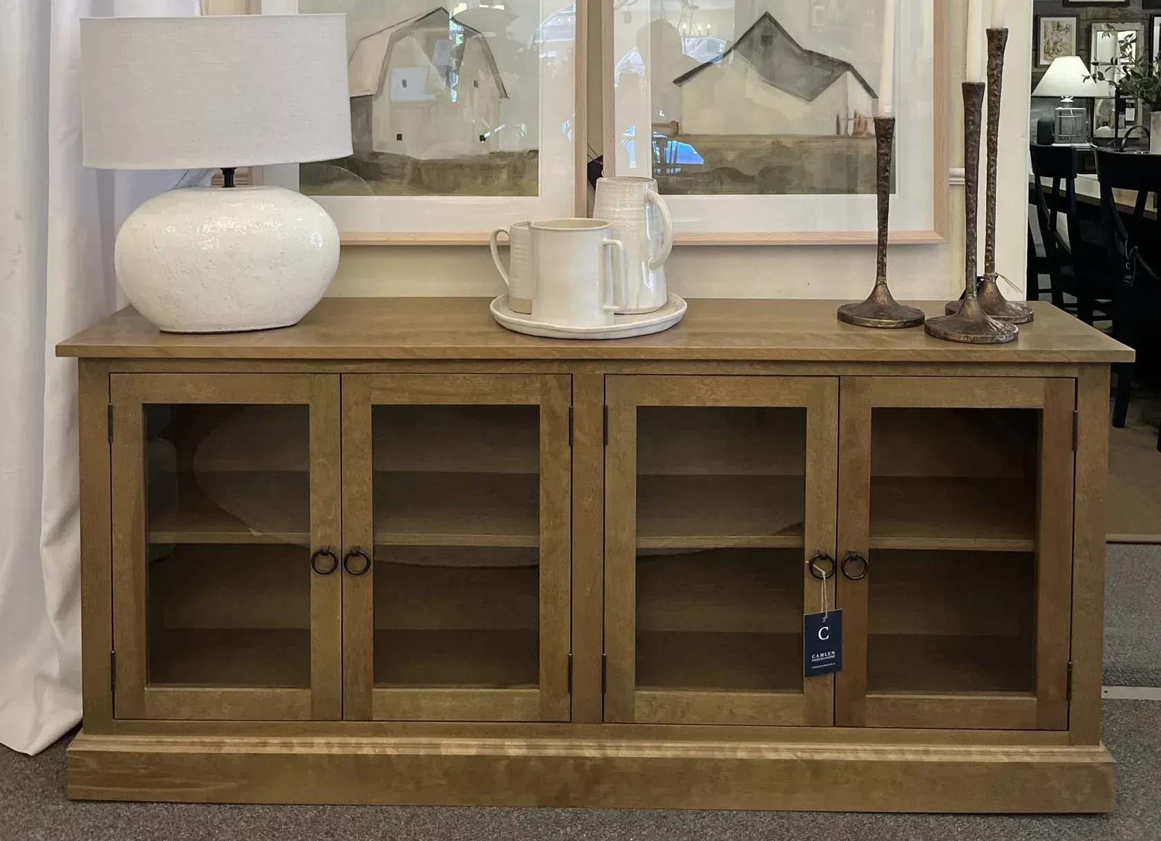 Wooden cabinet with glass doors, lamp, art, and decor.