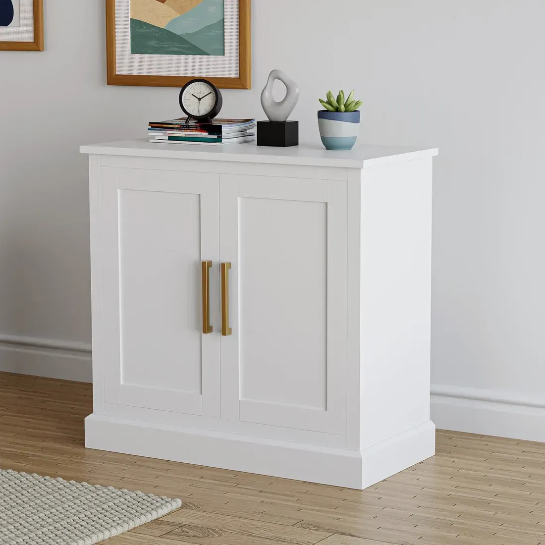White cabinet with gold handles, topped with decor against a wall.