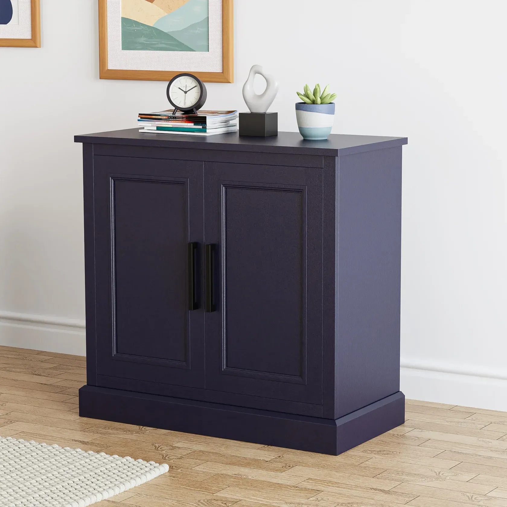 Dark blue cabinet with black handles, topped with decor: books, clock, sculpture, plant.