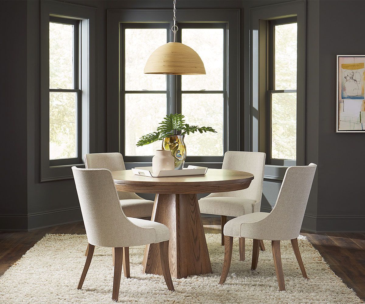 Dining room with round wooden table, four chairs, and large windows. Beige rug.