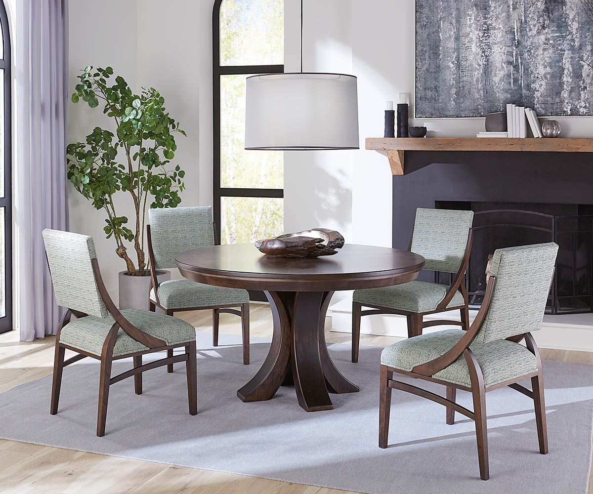 Dining room with round table and four chairs. Brown wood, light blue patterned upholstery, bright space.