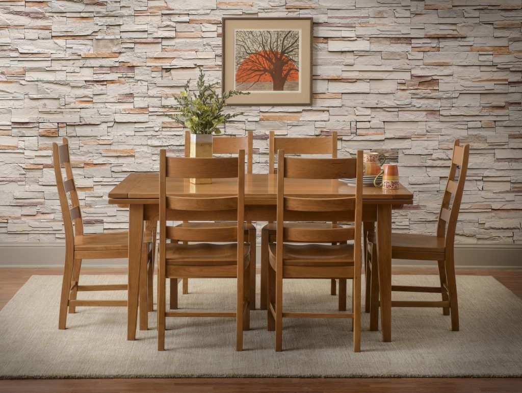 Wooden dining table and chairs set against a stone wall, topped with flowers and picture.