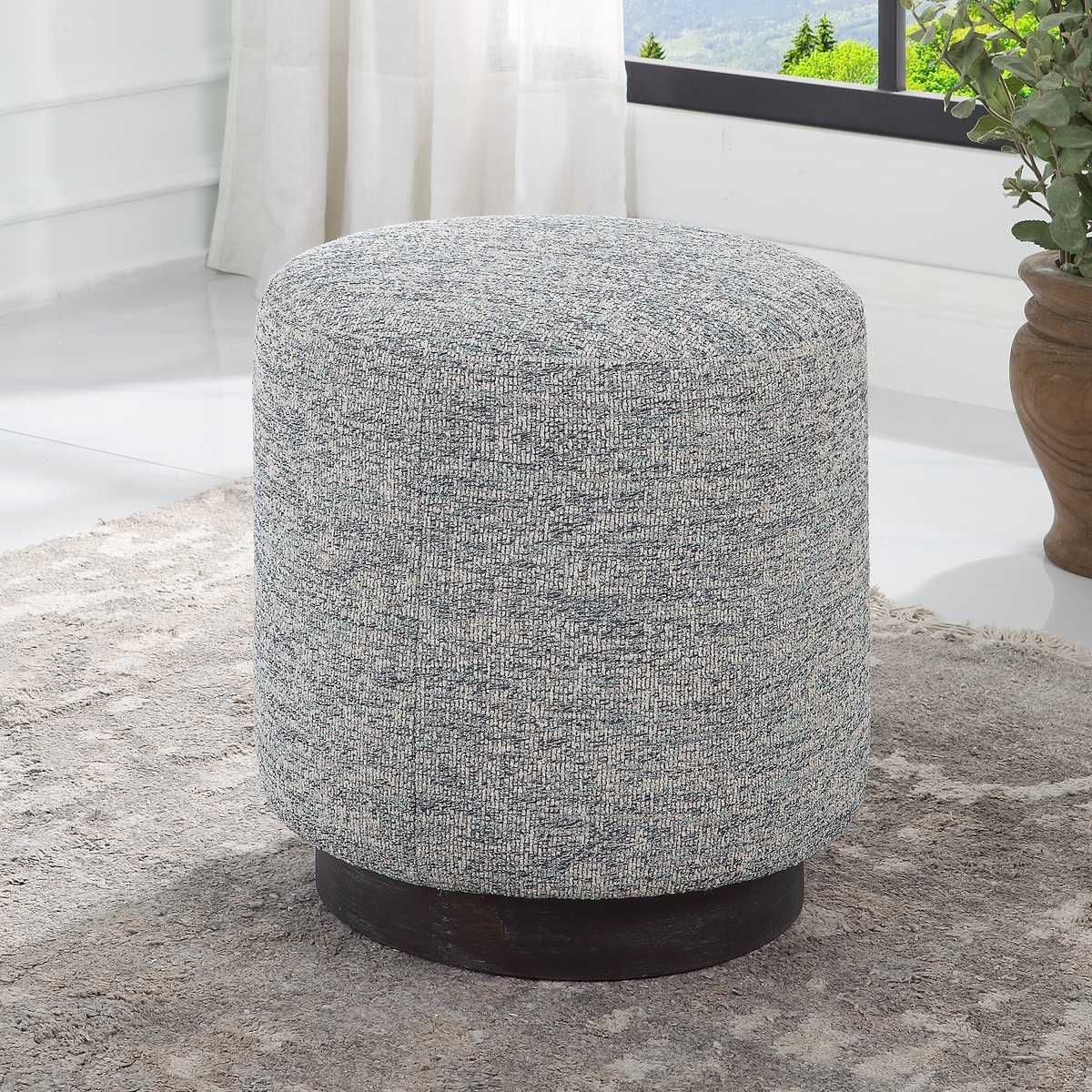 Round upholstered ottoman with gray and white fabric on a dark wooden base, set on a rug.