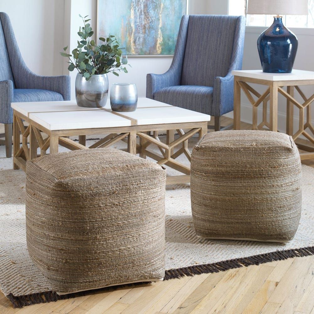 Two woven poufs on a rug in a living room with blue chairs and a white and wood coffee table.