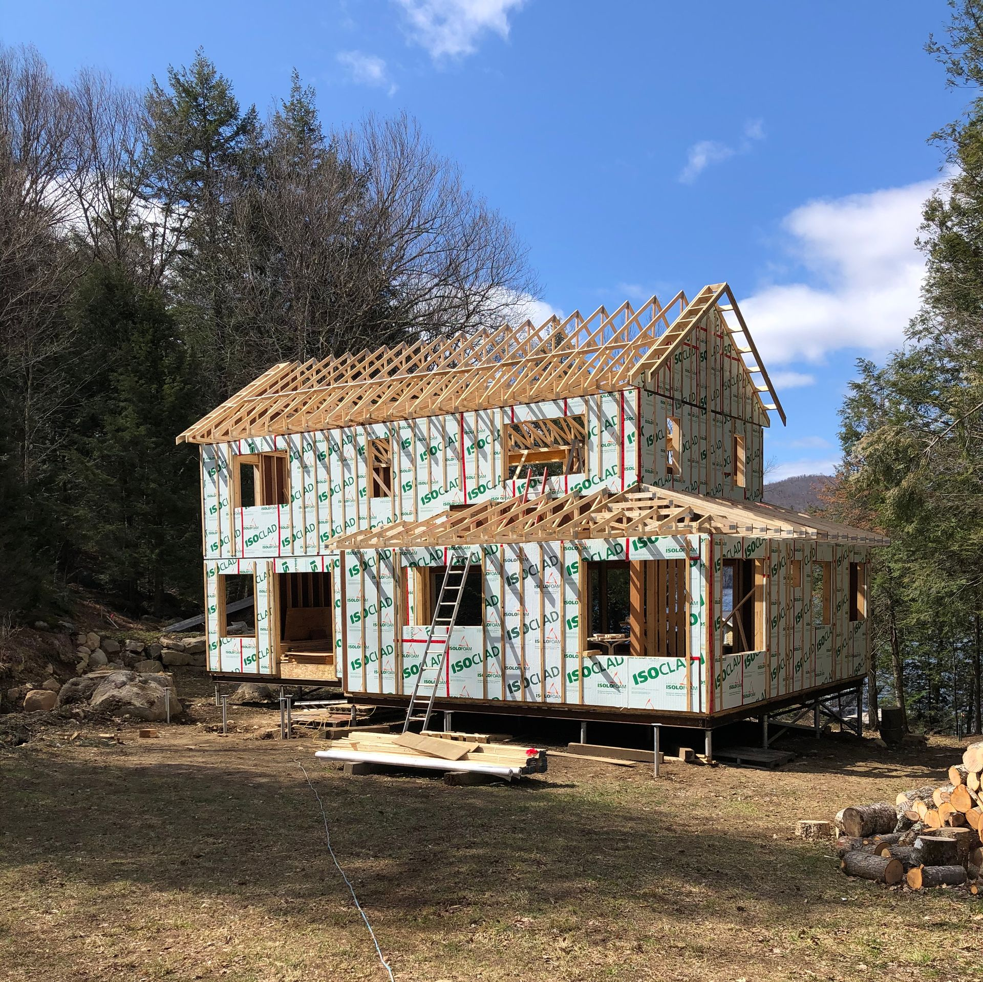 Une maison à deux étages en construction, à ossature de poutres en bois et recouverte d'un pare-vapeur protecteur vert et blanc.