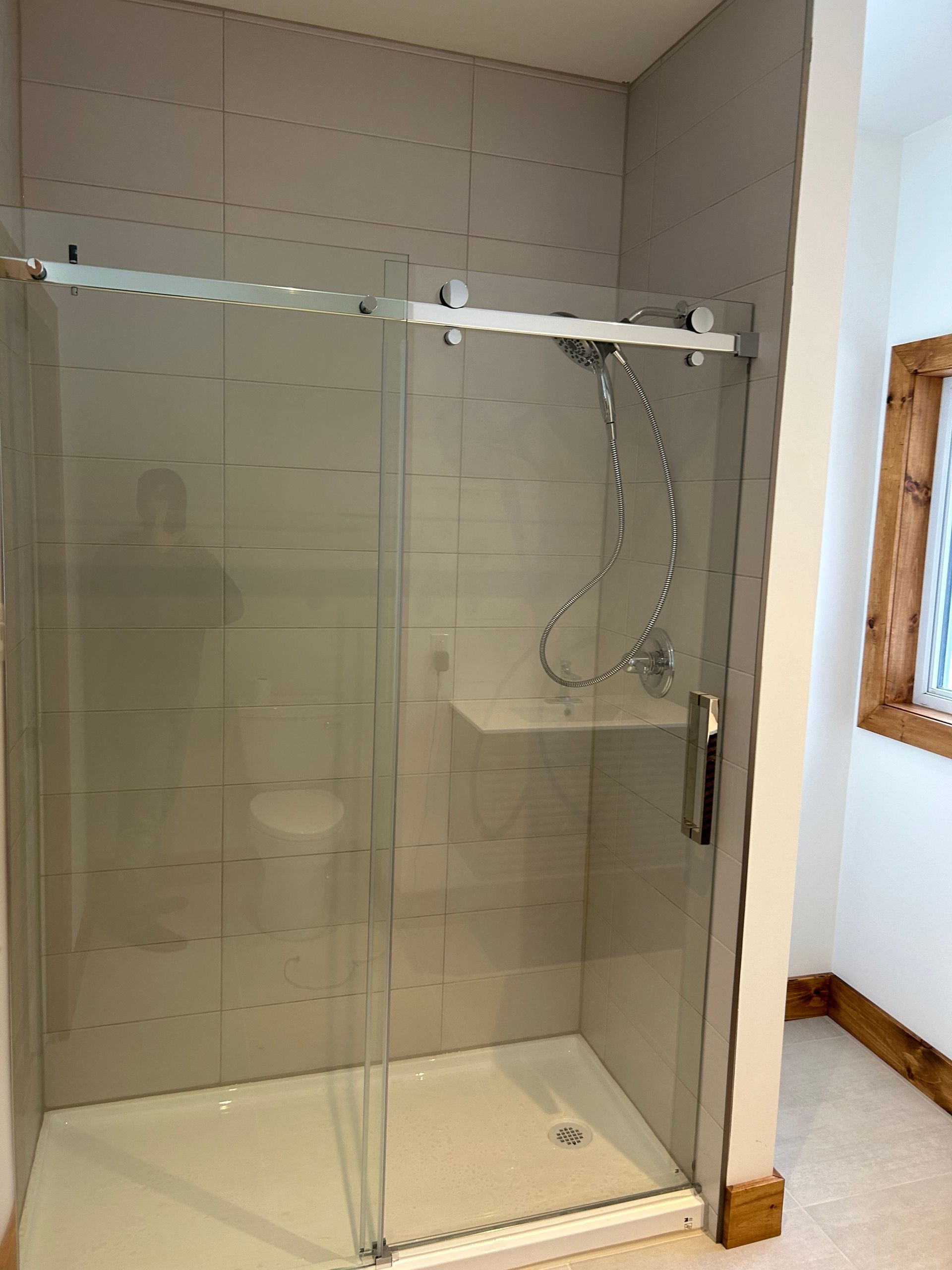 Une douche à l'italienne moderne avec porte coulissante en verre, murs carrelés gris clair et pommeau de douche chromé.