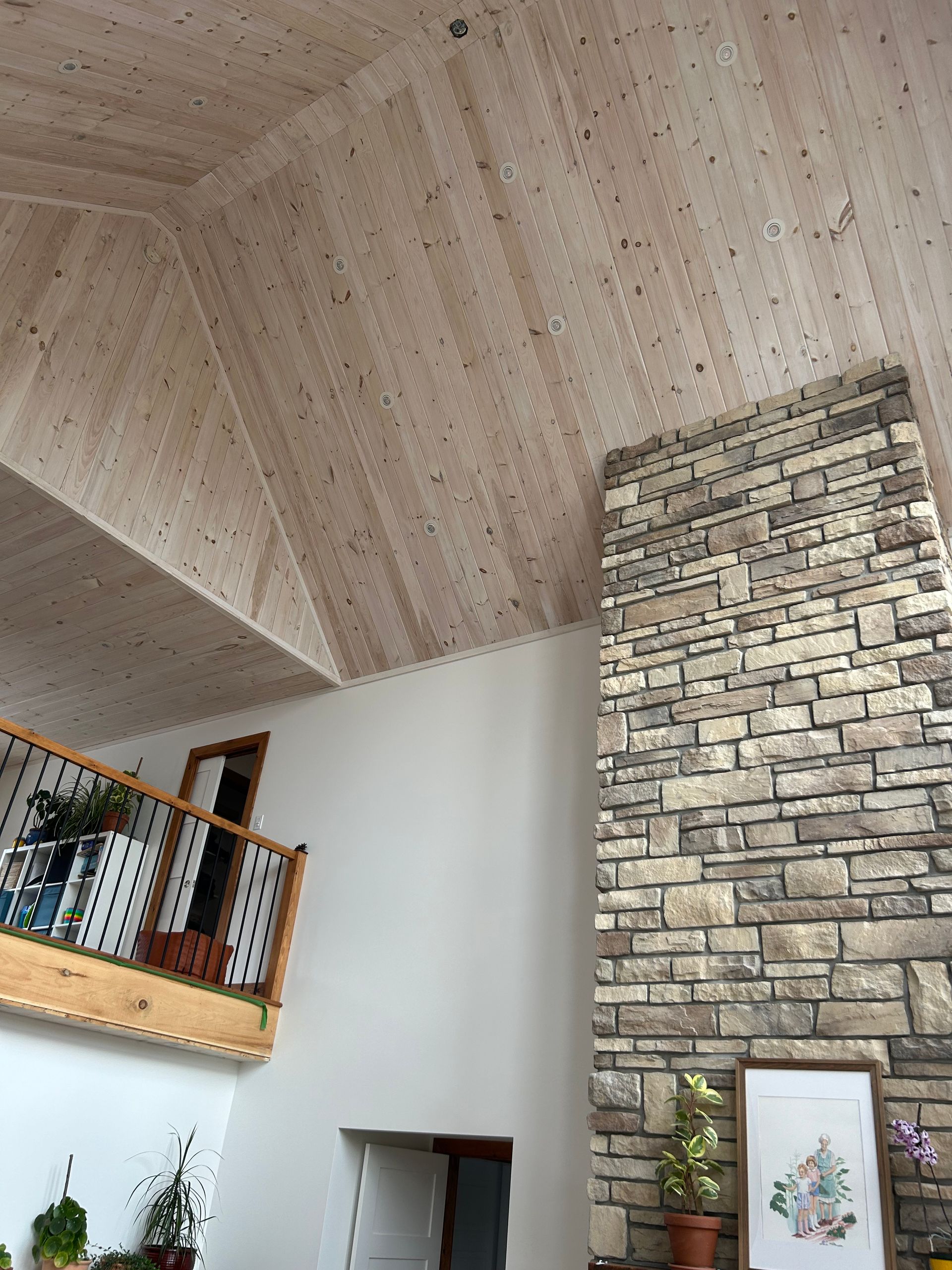 Une haute cheminée en pierre s'étend vers un plafond voûté en bois clair, à côté d'un balcon avec une balustrade en bois.
