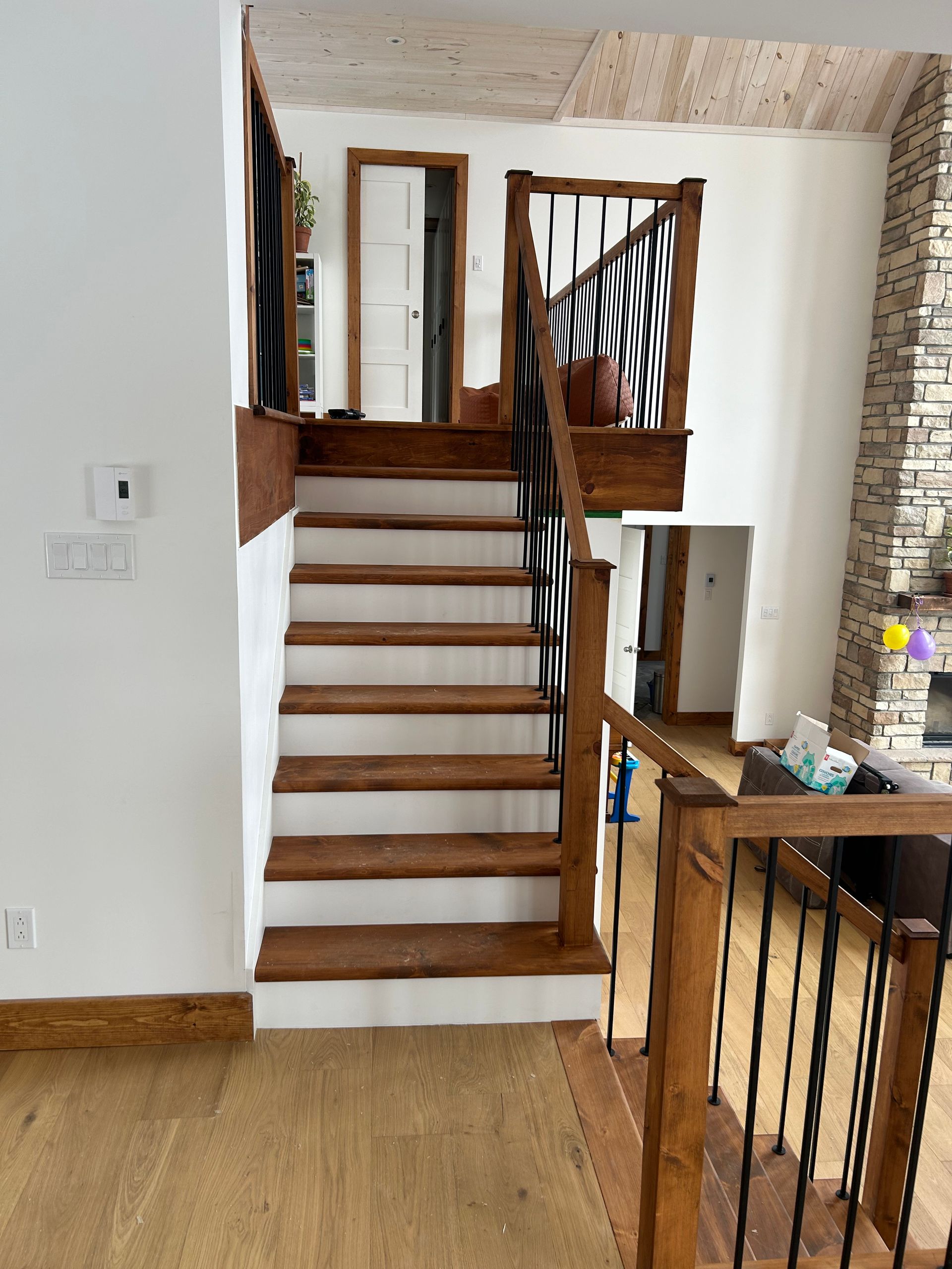 Un escalier en bois aux contremarches blanches et aux rampes en métal noir mène à un palier à l'intérieur d'une maison à plusieurs niveaux.