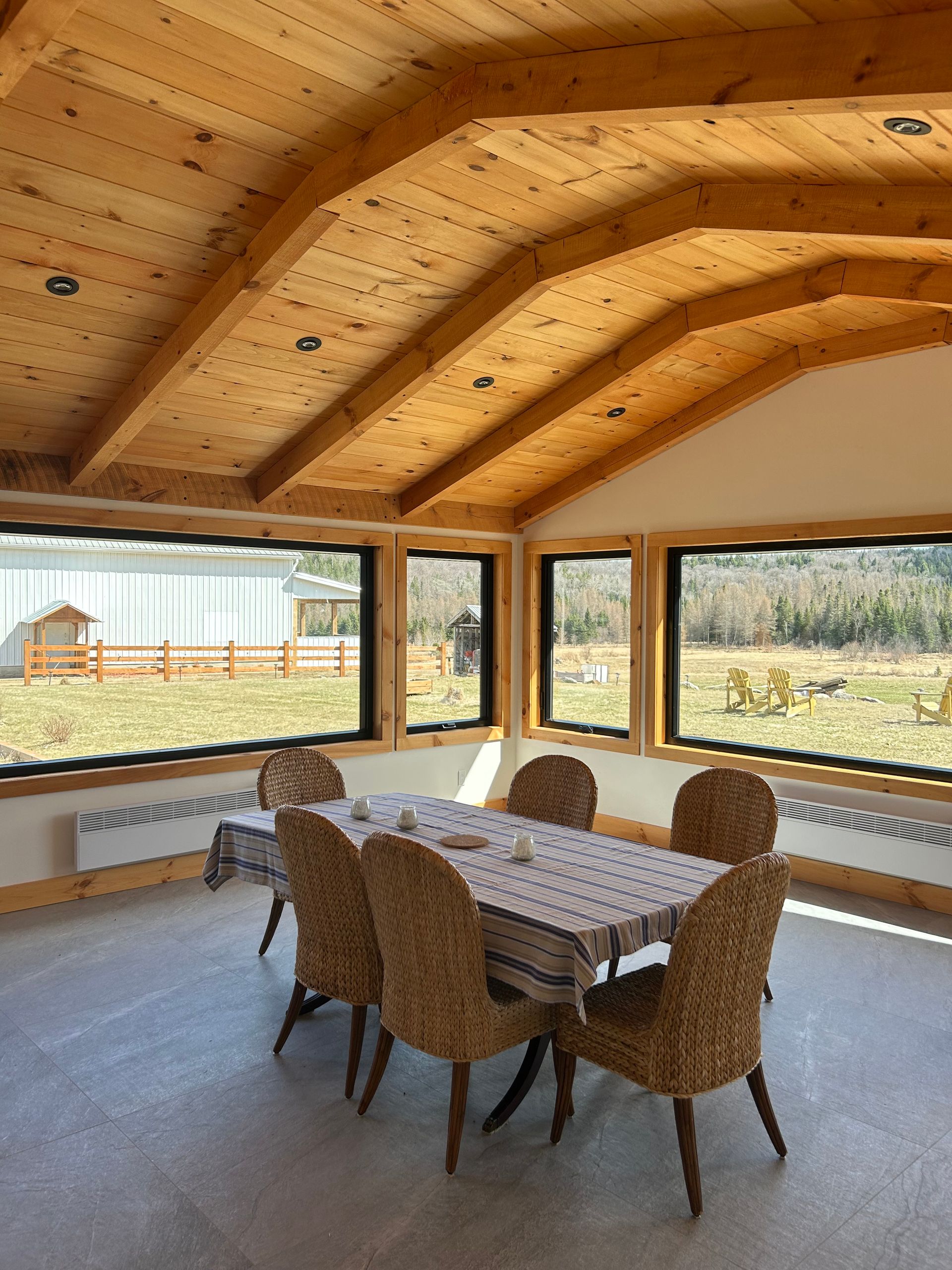 Une table à manger avec six chaises en osier dans une véranda dotée de plafonds voûtés en bois et de grandes fenêtres.
