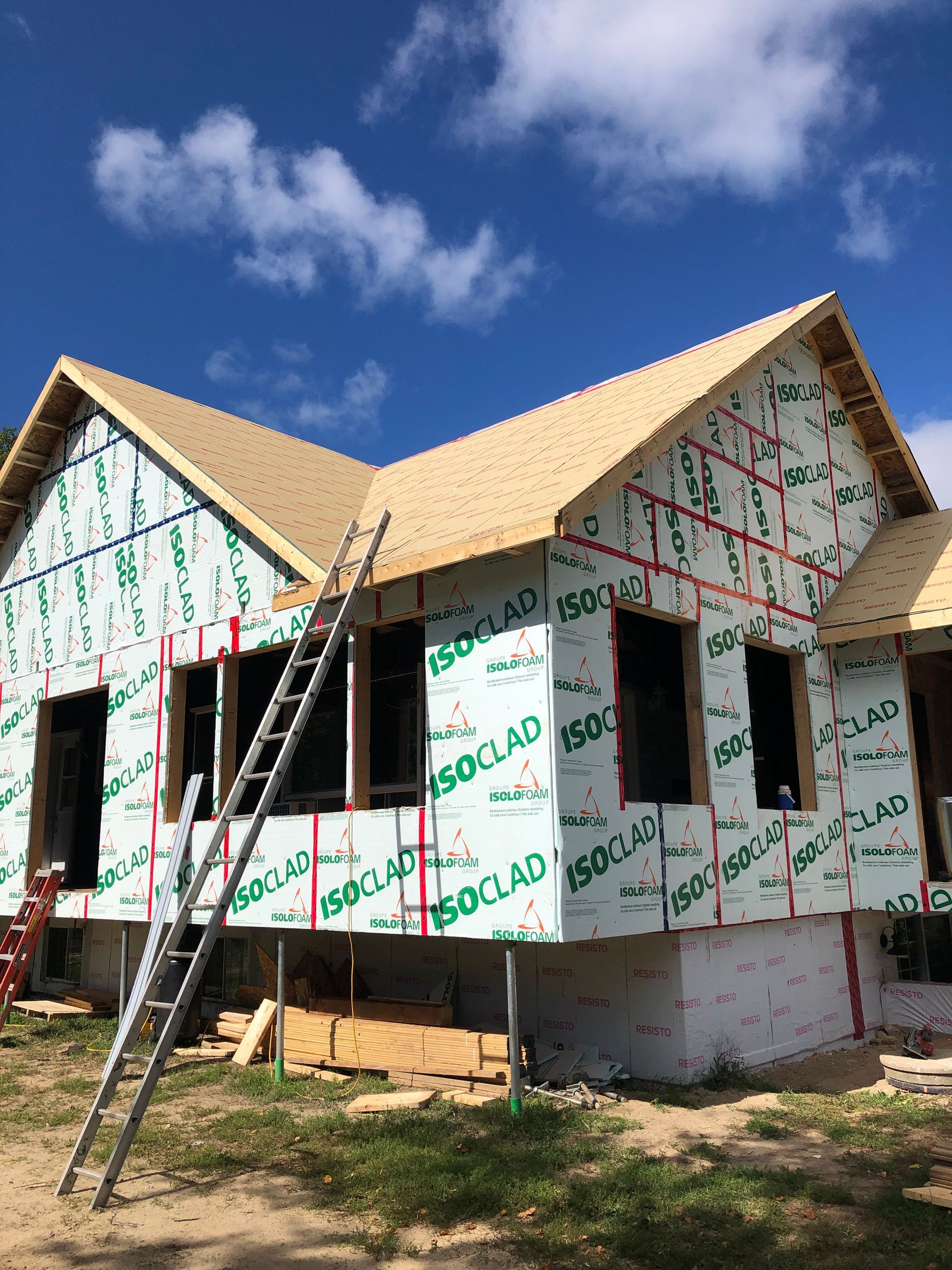 Une maison d'habitation en construction, recouverte de panneaux isolants Isoclad, avec une échelle métallique appuyée contre le mur.