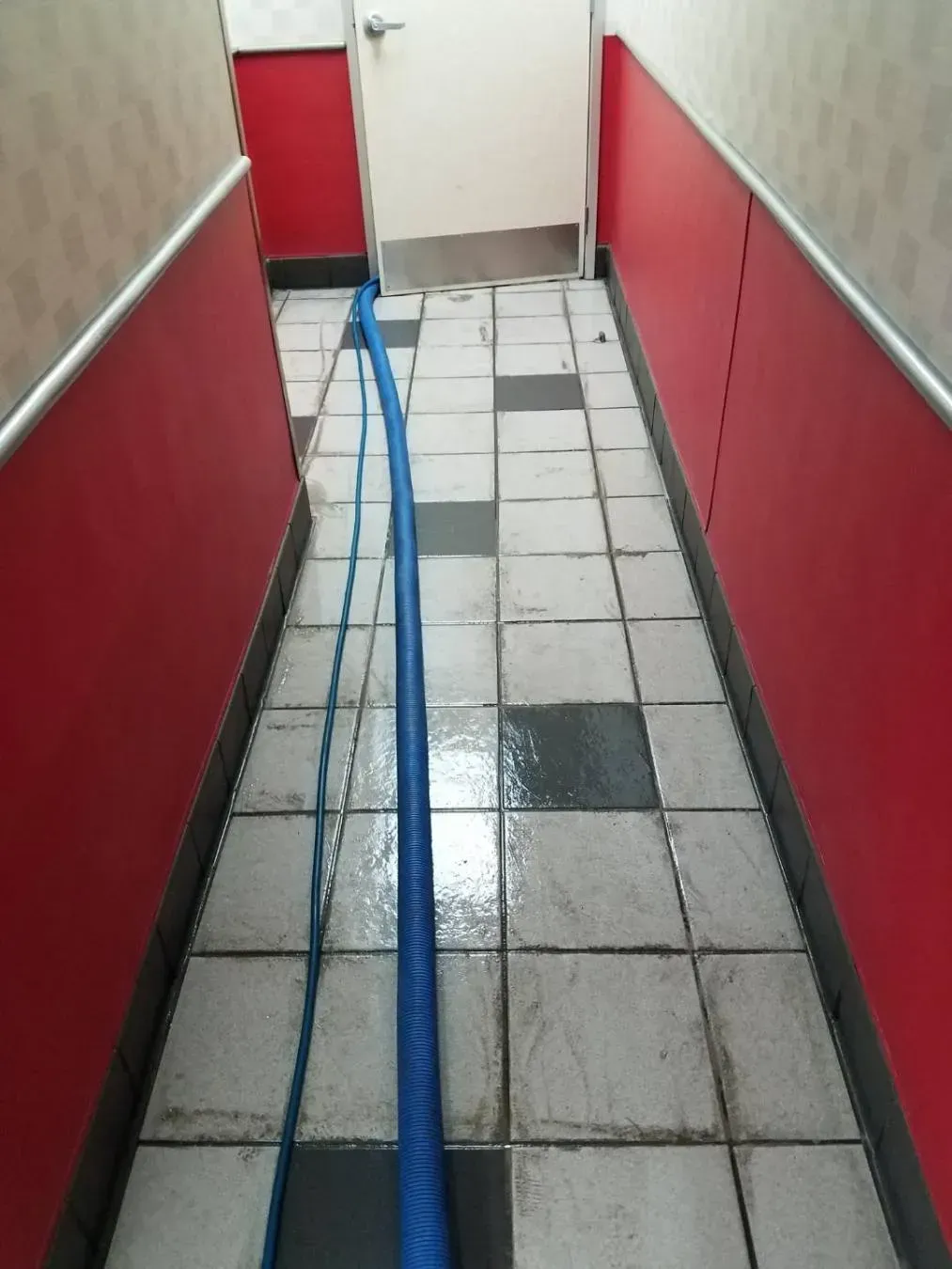 Blue hose on a wet tiled floor in a narrow hallway with red walls, leading to a door.