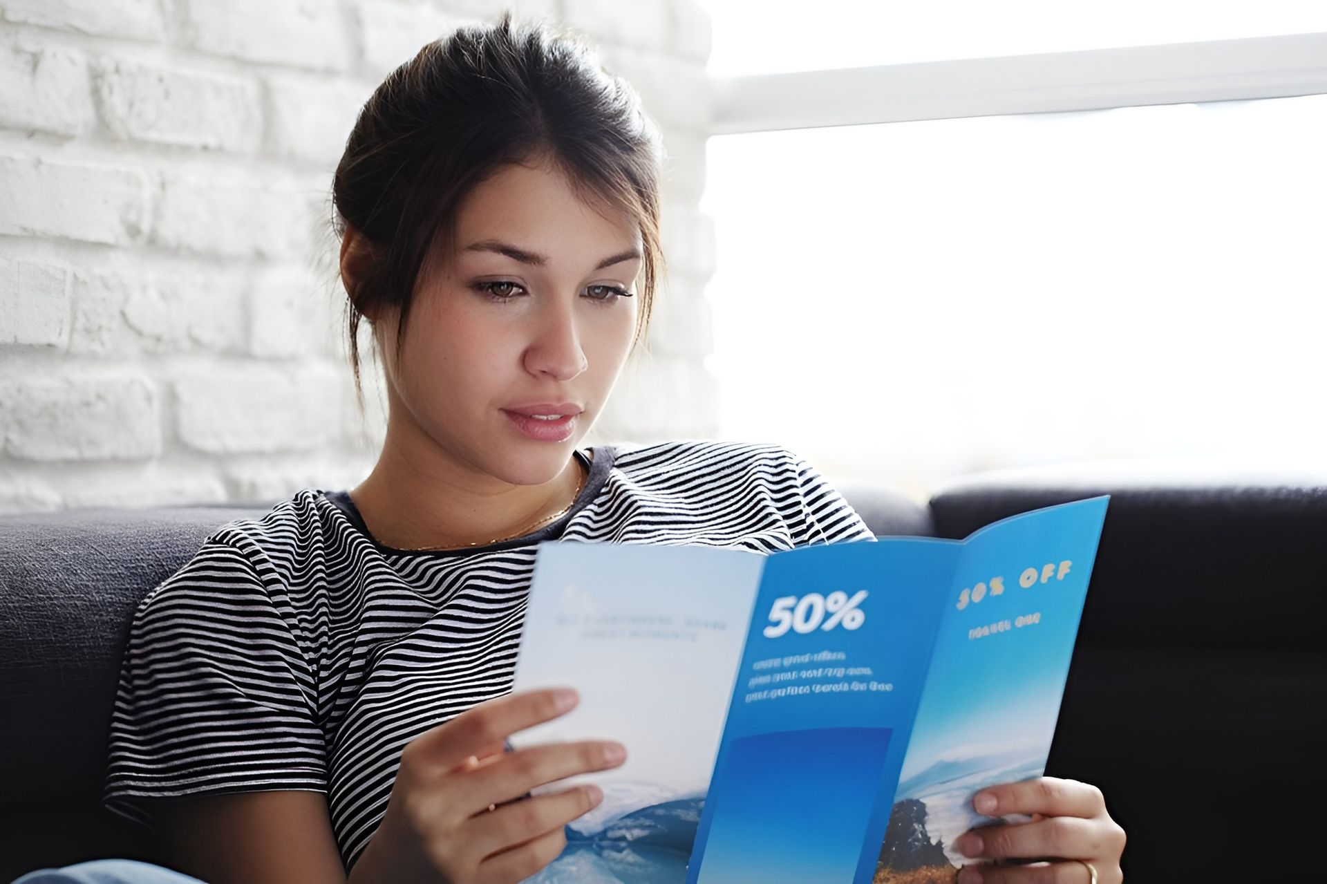 Woman Reading Brochure with 50% Off Text While Sitting on A Couch, Near a Window — Digi Print Pro in Bangalow, NSW