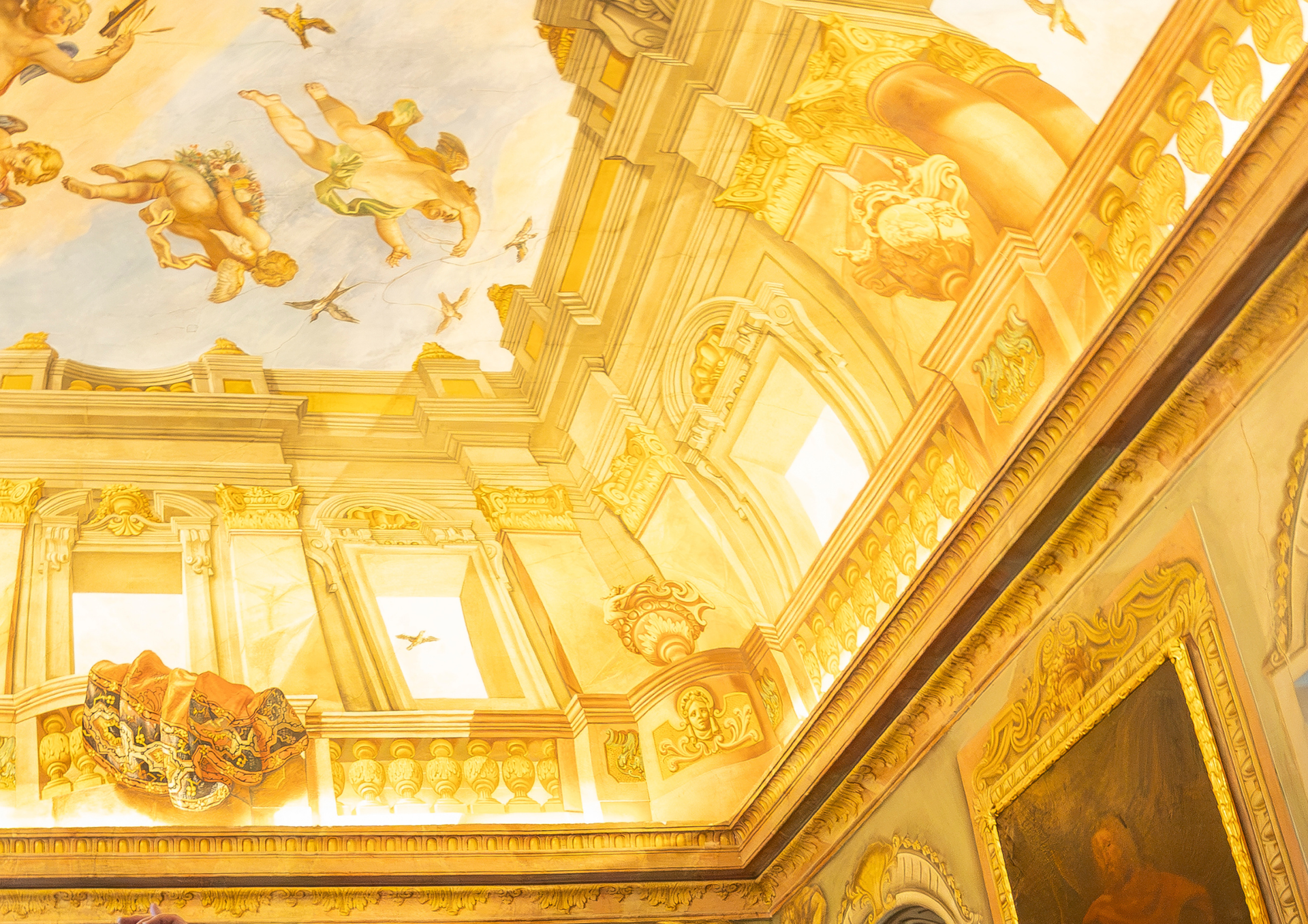 Prunkvolles, goldfarbenes Interieur mit gemalten Putten an der Decke, architektonischen Details und gerahmten Kunstwerken