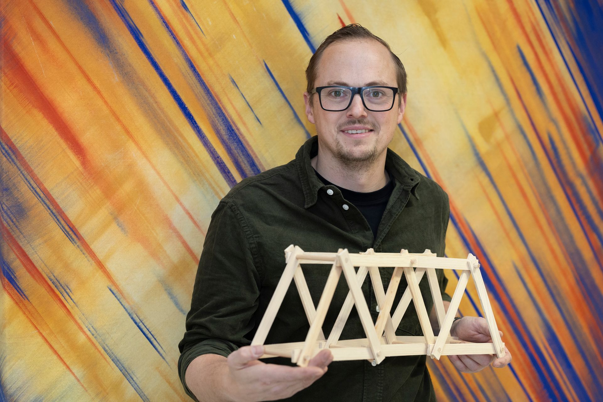 Männliche Person mit Brille hält Baukonstruktion aus Holz als Modell in der Hand