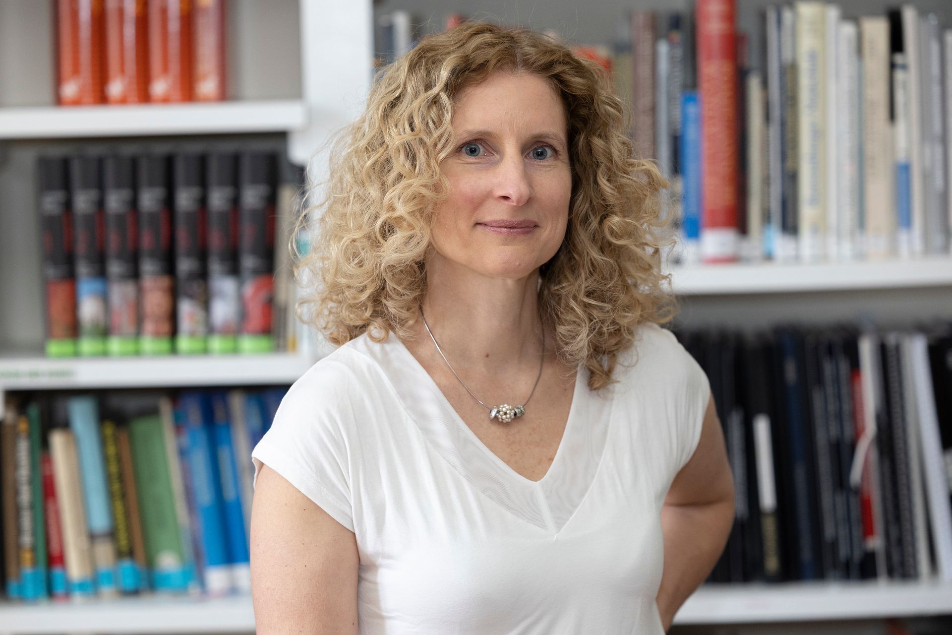 weibliche Person mit schulterlangen Haaren steht vor einer Bibliothek