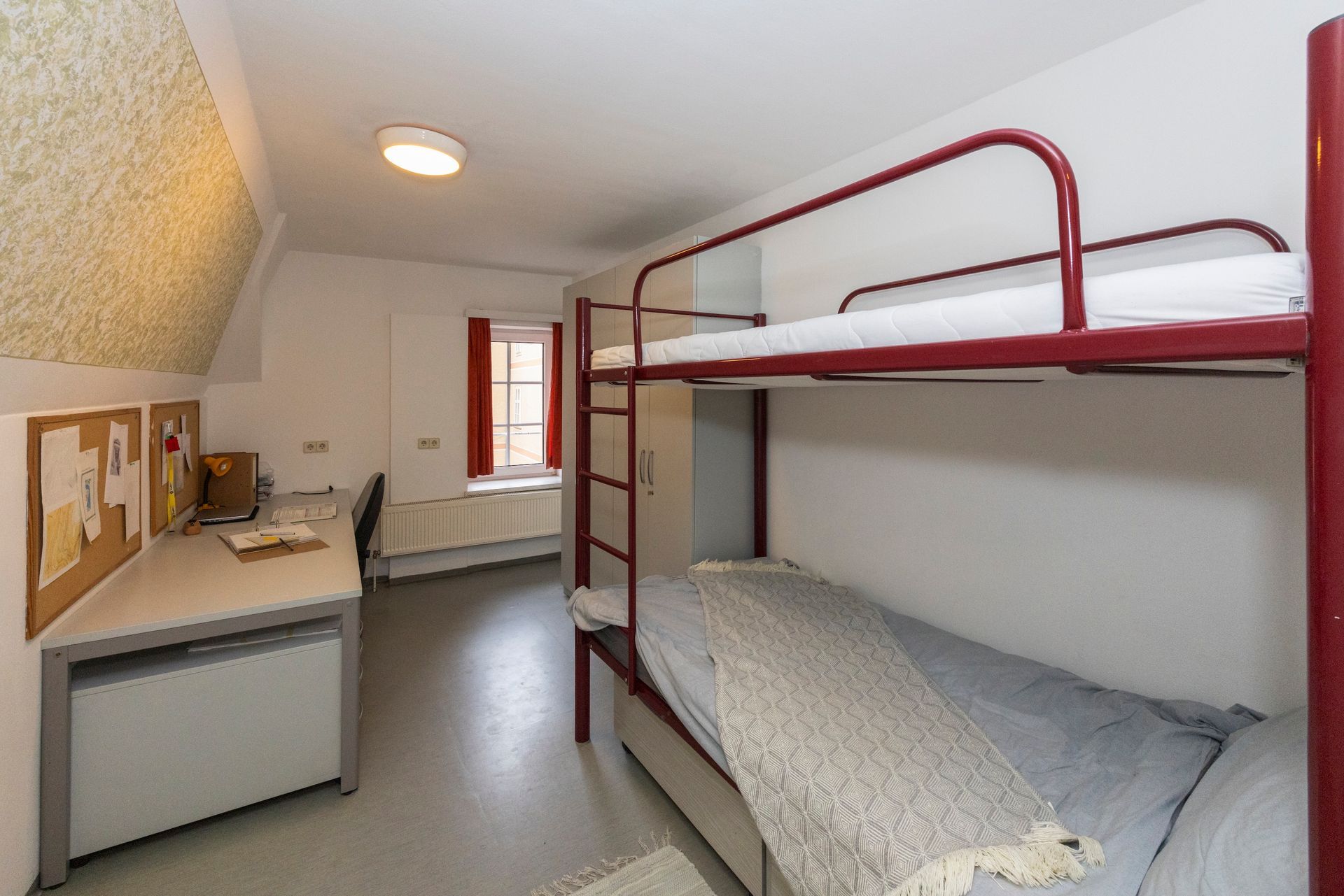 kleines, modernes Studentenzimmer mit einem roten Metall-Etagenbett, einem Schreibtisch .