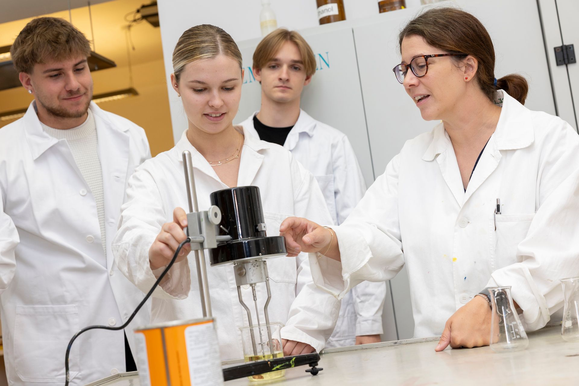 Lehrerin und drei Schüler in Laborkitteln führen in naturwissenschaftlichen Labor ein Experiment