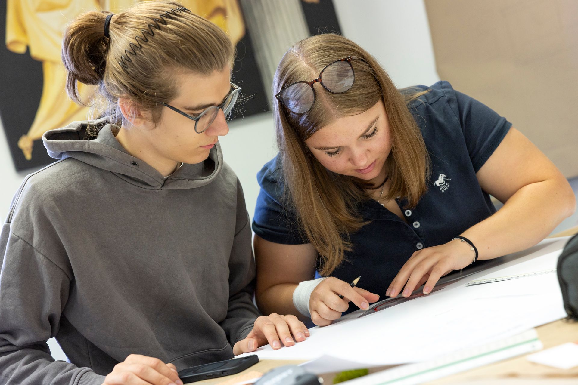 Zwei Schüler arbeiten zusammen an einem Schreibtisch und blicken auf ein großes Blatt Papier