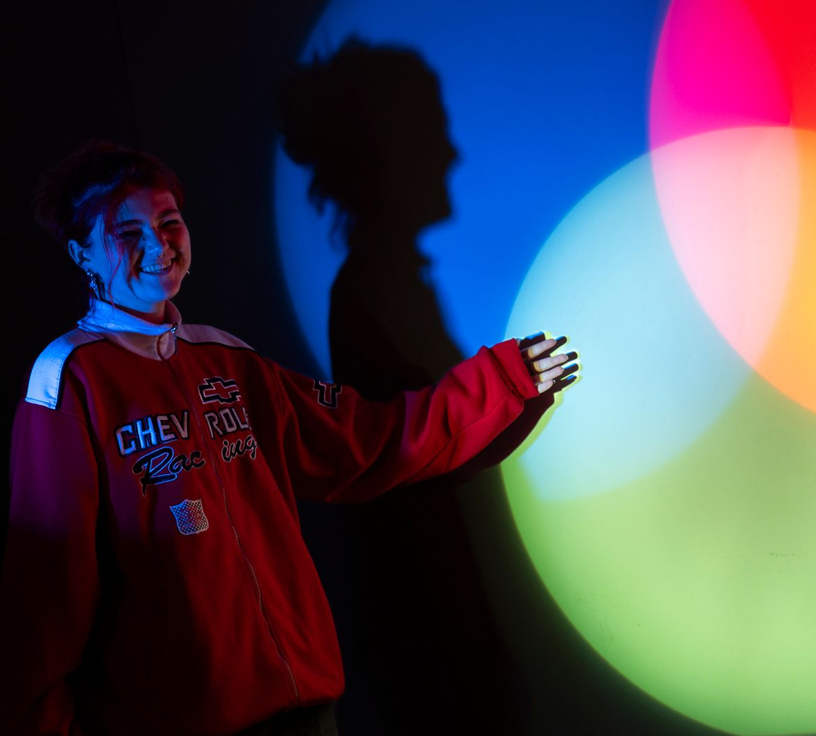 Person zeigt auf sich überlappende rote, blaue und grüne Lichtprojektionen an einer dunklen Wand