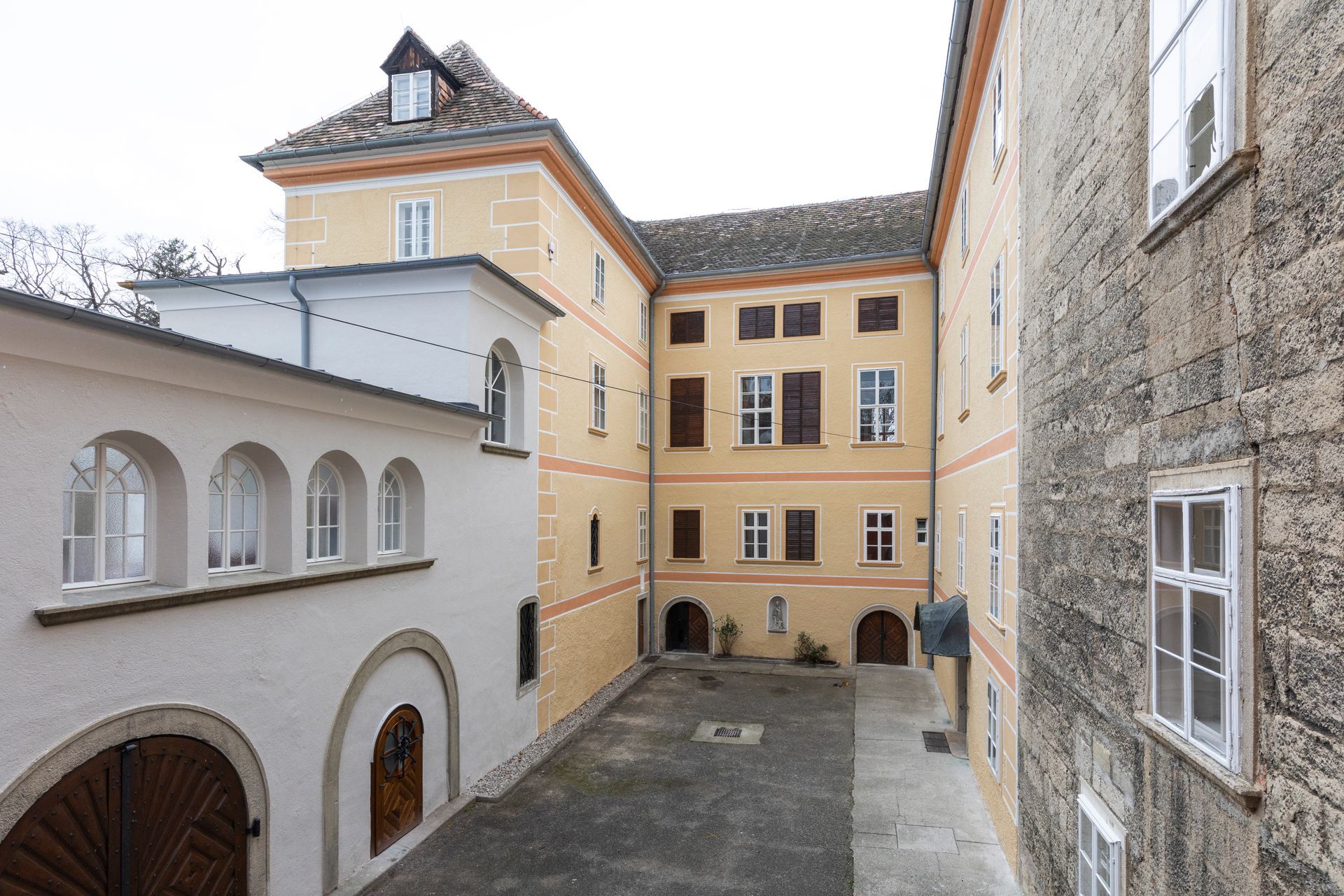 Innenhof eines historischen Steingebäudes mit gelber Fassade, Bogentüren und symmetrischen Fenstern