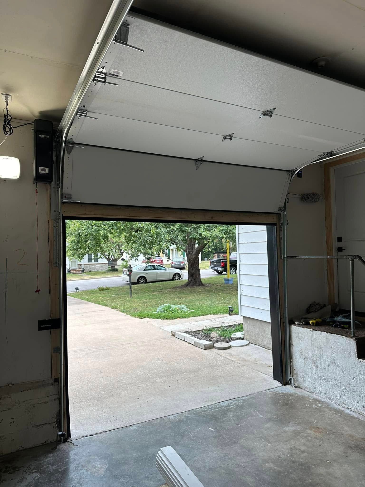 View through an open residential garage door looking out onto a residential street with a car parked on the driveway.