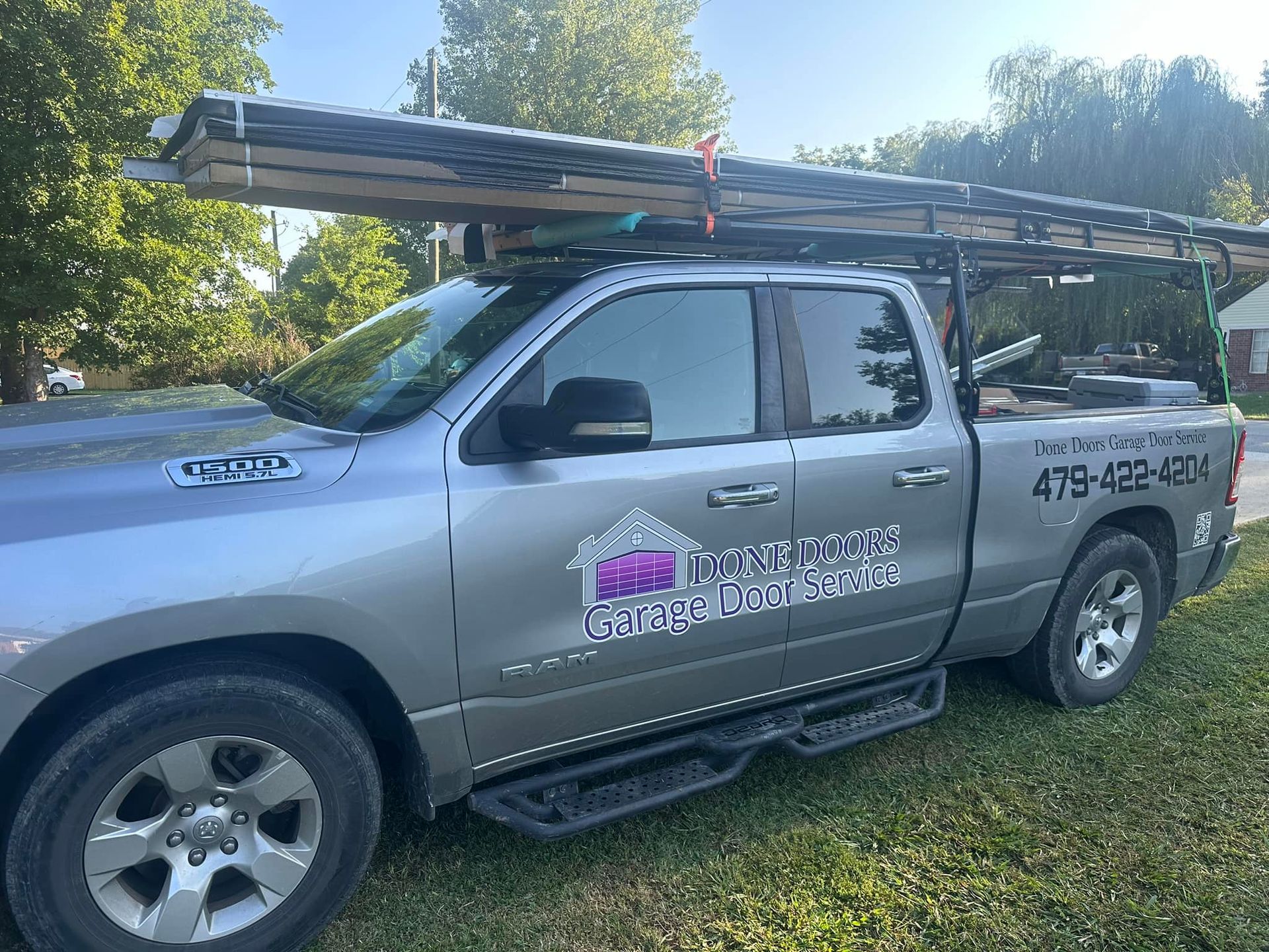 A silver crew-cab pickup truck with a roof rack carrying construction materials and a business logo on the door.