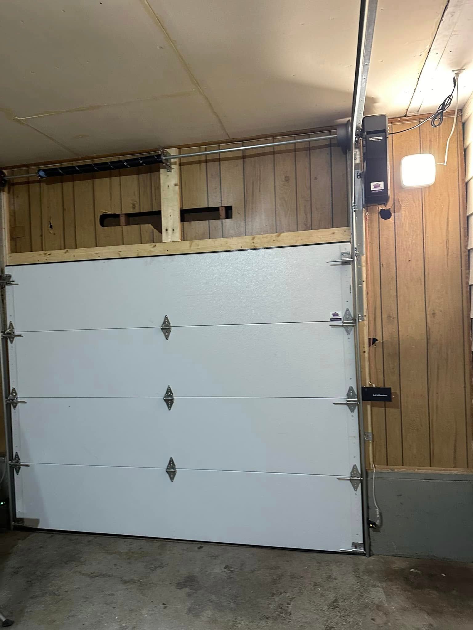 A white sectional garage door installed in an interior garage space with wood paneled walls.