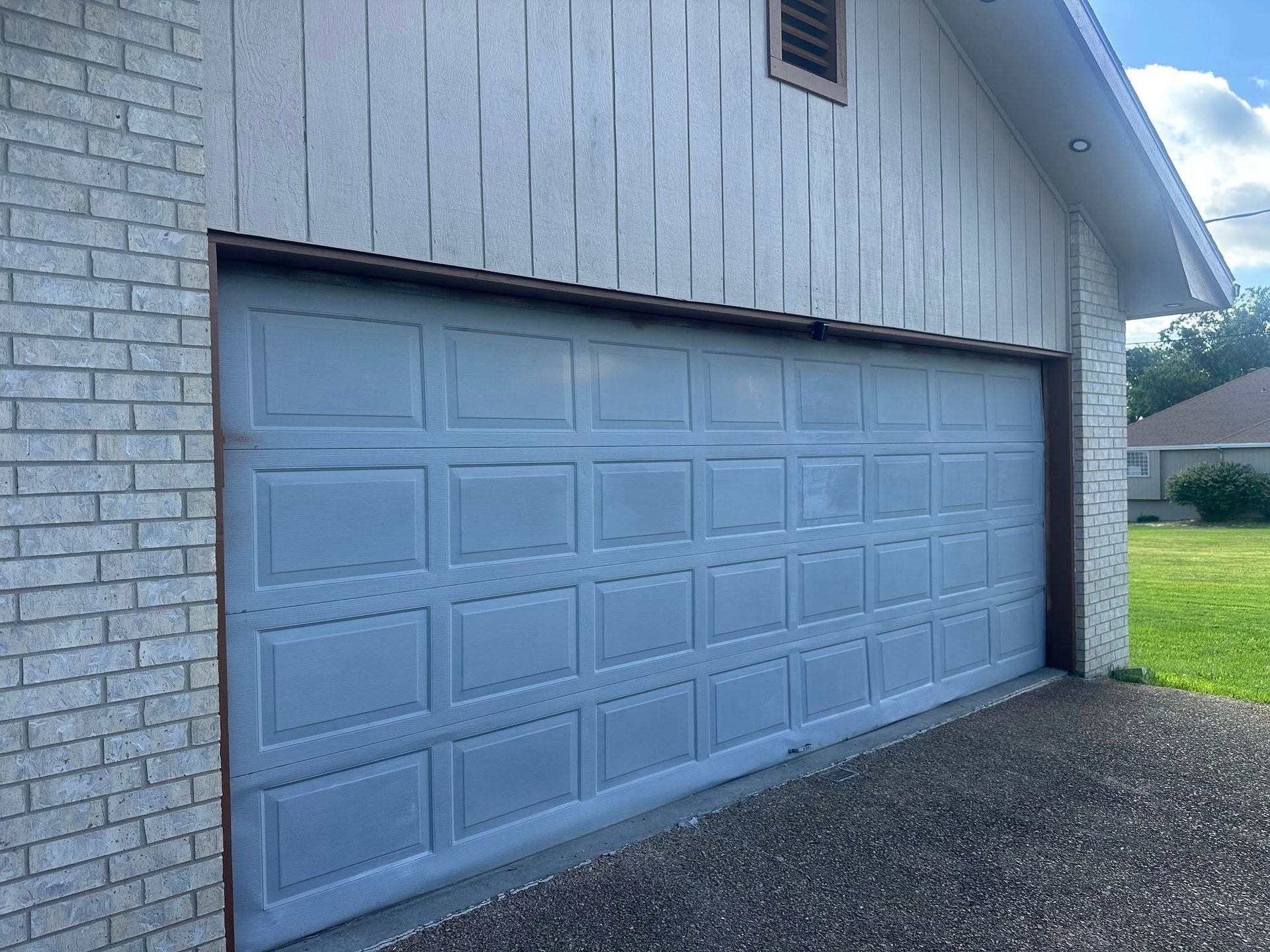 A light gray garage door set into a brick exterior wall with vertical wood siding above it.