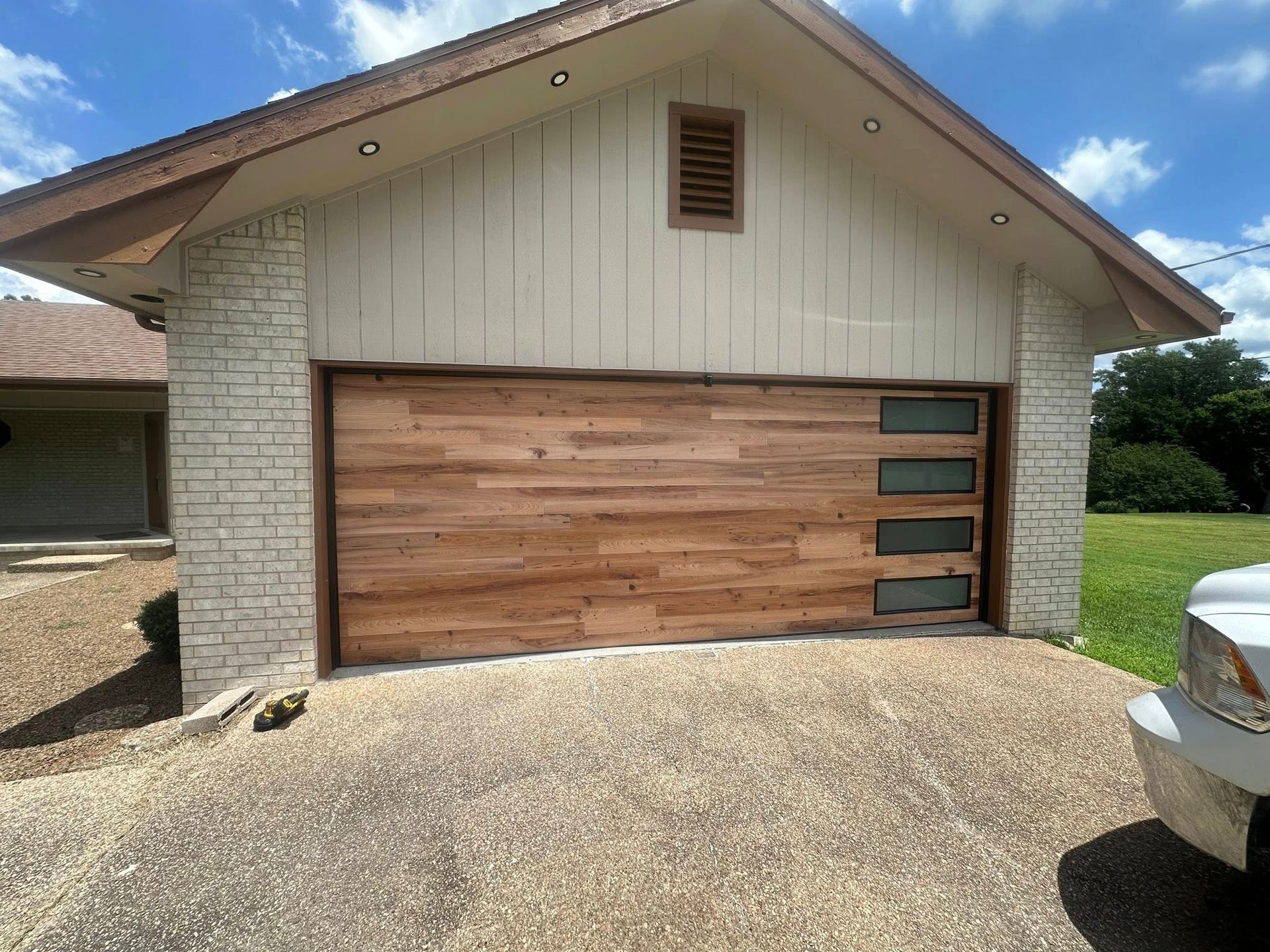 A garage with a natural wood-plank door featuring four horizontal windows, set between stone-textured pillars.