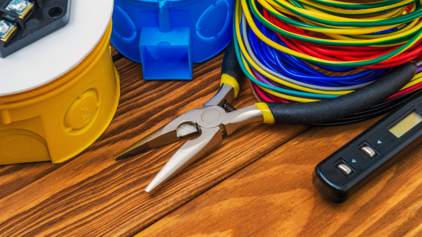 Wire cutters and coiled multicolored cables on a wooden workbench with electrical tools