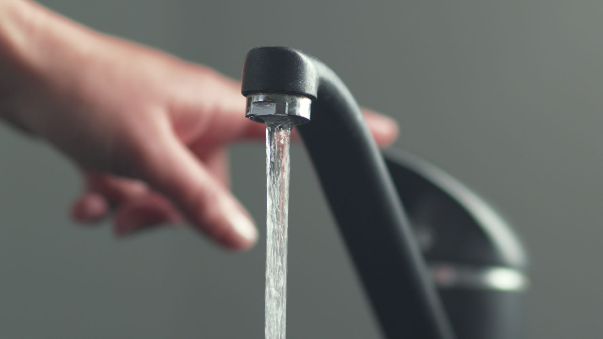 Water flowing from a kitchen faucet with a hand reaching toward the running stream.