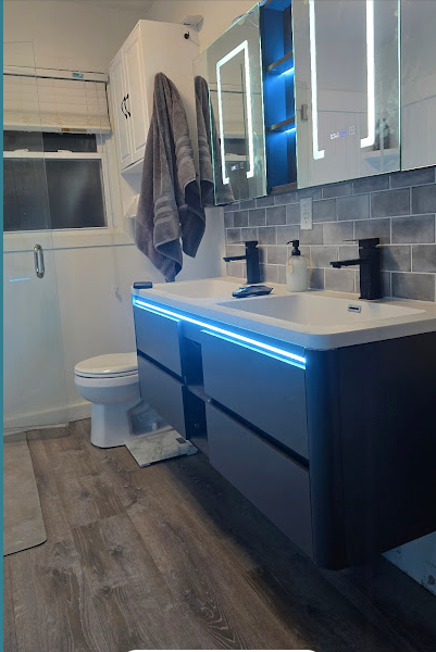 Modern bathroom with blue LED-lit vanity, double sink, mirror cabinet, towel, toilet, and window.