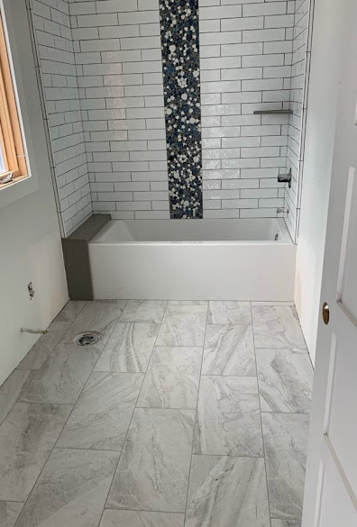 White-tiled bathroom with a walk-in tub, marble floor, and pebble accent strip in the shower area