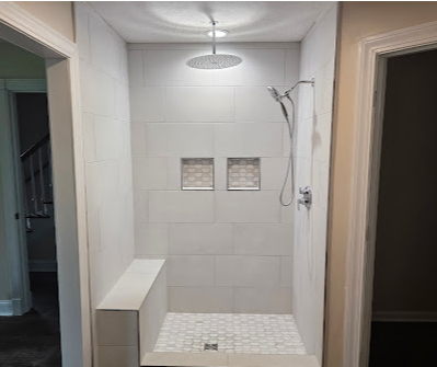 Walk-in shower with white tile, bench, mosaic floor, and chrome showerhead in a hallway opening