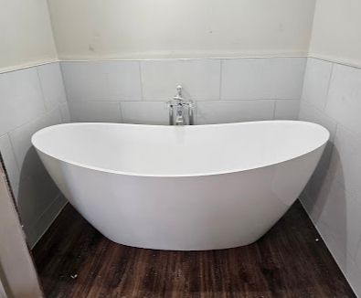 White freestanding bathtub in a tiled bathroom corner with dark wood flooring