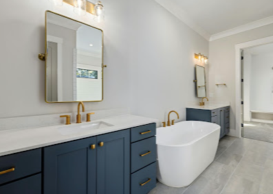 Modern bathroom with navy vanity, gold fixtures, and freestanding white tub