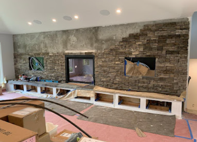 Living room with stone fireplace wall, white built-in TV console, and taped-off flooring during renovation