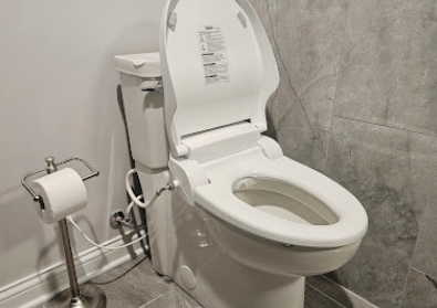 Accessible toilet with raised seat, bidet controls, and toilet paper holder in a tiled bathroom