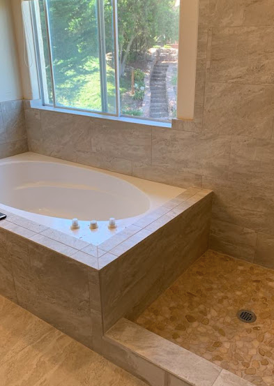 Bathroom with white soaking tub beside tiled walk-in shower and a window view outside