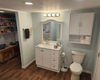 Small bathroom with vanity, mirror, wall cabinet, toilet, and wood-look flooring.