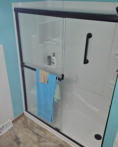 Glass shower enclosure with black frame and blue towel hanging on the door