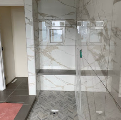 Modern bathroom with marble walls, glass shower enclosure, and gray herringbone tile floor